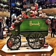 a green wagon filled with teddy bears on top of a wooden floor next to other people