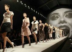 models walk down the catwalk in front of a large screen with a woman's face on it