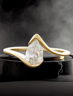 a ring with a pear shaped diamond in the center on top of a black surface