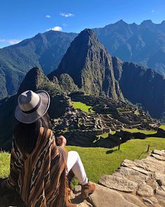 a woman sitting on the edge of a cliff looking at machu picach ruins