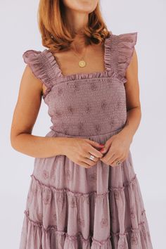 Float through your day in the charming Moody Dress! With flower embroidery, a smocked bodice, and ruffle sleeves, you'll feel as pretty as a petunia in this mauve dress. Perfect for any occasion, this dress is sure to make you feel as lovely as a spring day. Details Flower embroidered Smocked bodice Ruffle sleeves Sizing Approximate measurements: SIZE LENGTH BUST Small 45" 28" Medium 46" 30" Large 47" 32" Fabric has stretch in the bodice Model is 5’10 wearing small Material 100% PolyesterHand wa Flutter Sleeve Smocked Dress With Ruffles For Garden Party, Spring Dresses With Ruffled Straps In Purple, Spring Purple Dresses With Ruffled Straps, Feminine Smocked Dress With Ruffles And Flutter Sleeves, Purple Dresses With Ruffled Straps For Spring, Spring Dresses With Smocked Bodice And Ruffle Sleeves, Flutter Sleeve Dress With Smocked Bodice For Garden Party, Purple Spring Dresses With Ruffled Straps, Feminine Dress With Smocked Back And Ruffle Sleeves