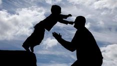 a silhouette of a man holding a child up in the air with clouds behind him