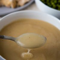 a spoon full of soup with broccoli in the background and another bowl behind it