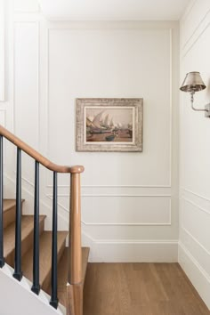 a painting hanging on the wall next to a stair case in a white walled room