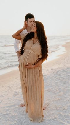 a pregnant woman standing on the beach with her husband