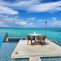 a table and chairs sitting on top of a pool next to the ocean with an umbrella