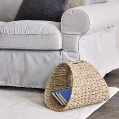 a basket sitting on the floor in front of a white couch with black and blue pillows