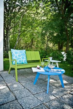 two green and blue benches sitting next to each other on a stone patio with trees in the background