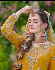 a woman in yellow dress with jewelry on her head and hands behind her head, looking to the side