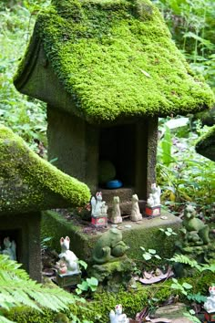 a moss covered birdhouse in the middle of a forest filled with figurines