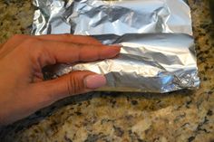 a hand holding aluminum foil over a piece of food on top of a granite counter