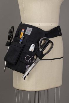 a black belted bag with scissors and other items in it on top of a mannequin