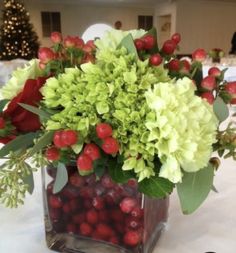 a vase filled with green and red flowers on top of a white tablecloth covered table