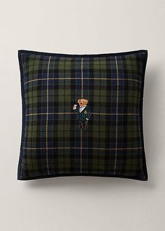 a black and green plaid pillow with a teddy bear on the front, sitting against a white wall