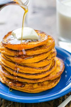 a blue plate topped with pancakes covered in syrup and being drizzled with butter