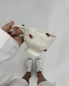 a person is holding a white cup with ladybugs on it and their feet are in the air