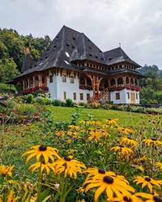 a large white house sitting in the middle of a lush green field with lots of yellow flowers