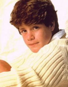 the young boy is wearing a white sweater and posing for a photo with his arms crossed