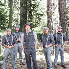 a group of men standing next to each other in front of some trees with suspenders