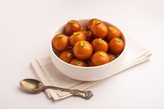 a white bowl filled with oranges on top of a napkin next to a spoon