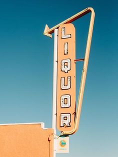 an old neon sign for a liquor store on the side of a building in front of a blue sky