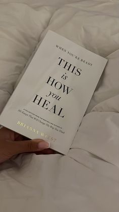 a person is holding up a book about how to heal on a bed with white sheets