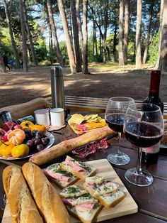 a picnic table with bread, cheeses and fruit on it next to a glass of wine