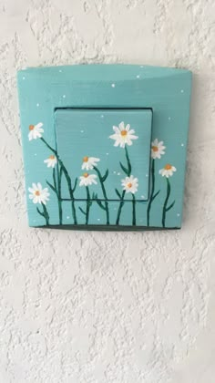 a blue light switch cover with daisies painted on the front and back side, in french