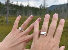 two hands holding each other in front of a field with trees and mountains behind them