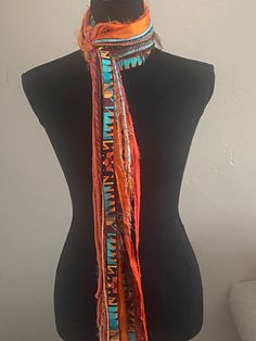 "This handmade scarf consists of a variety of yarn strands and hand sewn fabric ribbon in lovely southwest colors, orange rust yellow brown and turquoise.  I utilize a variety of yarns in each of my scarves and no two are ever the same.   Each scarf is made up of a selection of Sari Silk, Eyelash, Ribbon, Ladder, Fuzzy, Sparkly, Pouf Pom Pom, Boucle, Flag Ribbon, Nub, Pluscious, Hand Spun, and Brushbound. It is approximately 80\" long. This is an open fringe style, tied at center allowing for styling flexibility.  It is a medium weight scarf. Check out this YouTube link for a demonstration of the many ways that you can style this scarf: https://www.youtube.com/watch?v=5LYAEz777AU" Bohemian Brown Scarves For The Beach, Bohemian Brown Scarves For Beach, Bohemian Brown Scarf For The Beach, Bohemian Orange Scarf For Beach, Bohemian Brown Scarf For Beach, Bohemian Weaving Scarf For Fall, Bohemian Woven Scarves One Size, Brown Bohemian Scarves One Size, Brown Bohemian Woven Scarf