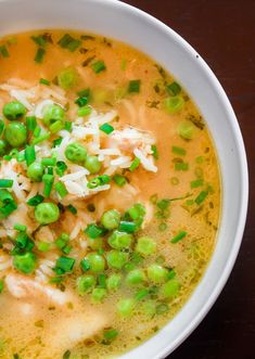 a bowl of soup with peas, rice and green onions on the top is sitting on a table