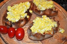 four baked potatoes with eggs and tomatoes on a wooden plate next to two cherry tomatoes