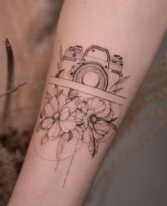 a woman's arm with a camera and flowers tattoo on the left side of her arm