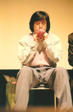 a man sitting in a chair while holding an apple up to his face with both hands