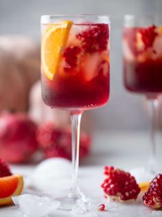 two glasses filled with red wine and garnished with oranges, raspberries and lemon wedges