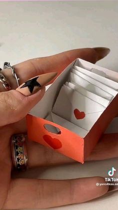 a hand holding an open red box with hearts on it and two rings around it