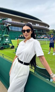 a woman standing on top of a tennis court next to a green wall with people in the background