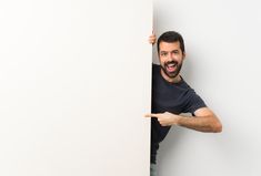 a man is peeking out from behind a white wall and pointing his finger at the corner