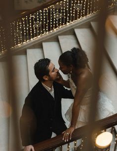 a man and woman standing on top of a stair case next to each other with lights in the background