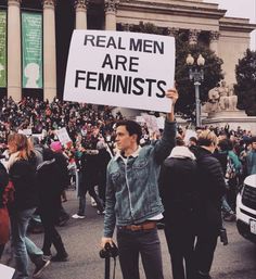 a man holding up a sign that says real men are feminists in front of a crowd