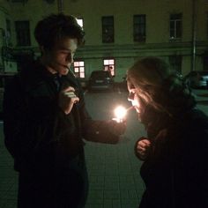 two people standing in front of a building with their lights on