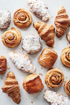 many different types of pastries on a white counter top with powdered sugar and sprinkled croissants