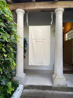 a white banner hanging from the side of a building next to some bushes and trees