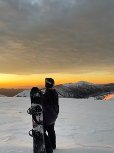 a person holding a snowboard on top of a snow covered slope with mountains in the background