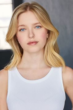 a woman with blonde hair and blue eyes wearing a white tank top looking at the camera