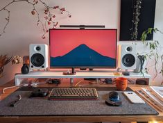 a desk with a computer, keyboard and speakers on top of it in front of a plant