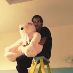 a man sitting on a stool holding a large white teddy bear in his right hand