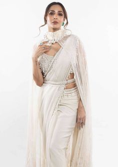 This feather cape sari set is a georgette sari, with a pearl embellished blouse, cape with feathers, and a belt. White Blouse With Sheer Dupatta For Party, White Party Blouse With Sheer Dupatta, Glamorous Pre-draped Saree With Cape Sleeves For Reception, Traditional White Pre-draped Saree For Evening, Glamorous White Pre-draped Saree For Festive Occasions, Bollywood Style White Evening Saree, White Bollywood Saree For Evening, Glamorous White Traditional Saree, Glamorous White Saree For Festive Occasions