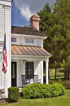 a white house with two rocking chairs on the front porch and an american flag hanging from the roof