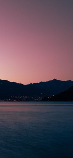 an airplane is flying over the water at night with mountains in the backgroud